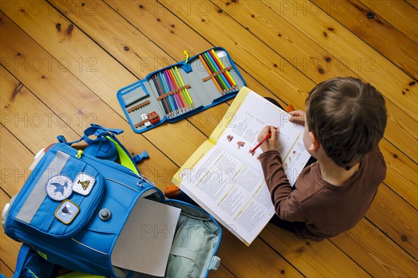 Symbolic photo on the subject of doing homework at home. A boy sits on the floor doing homework. Berlin