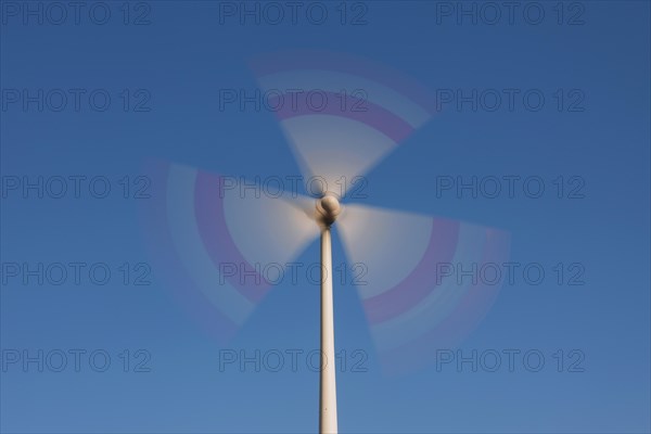 Spinning blades of wind turbine against blue sky