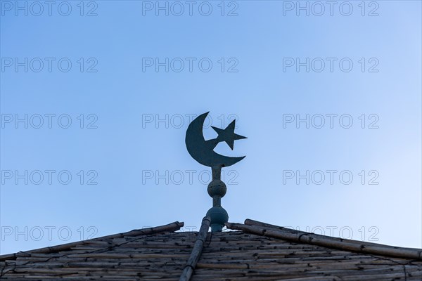 Cresecent moon and star symbol on roof against blue sky