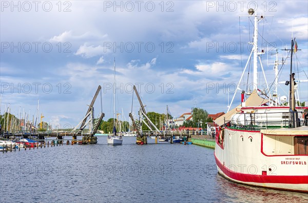 A sailboat is about to pass the old historic wooden bascule bridge in the city harbour of Greifswald-Wieck
