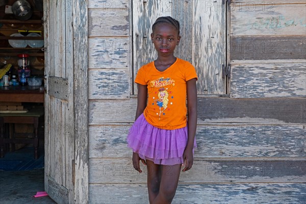 Portrait of young Afro-Surinamese girl with braided hair in front of wooden house in the village Aurora