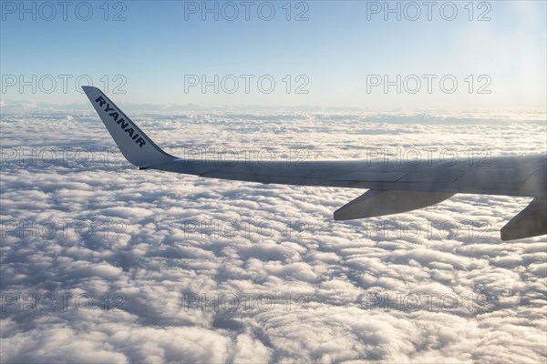Wing of Ryanair airline Boeing 737 plane flying at high altitude above clouds