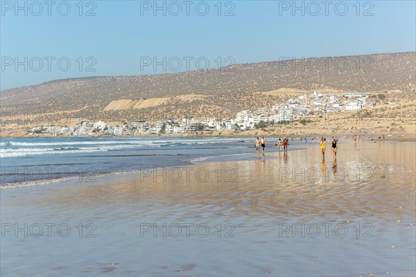 People walking along sandy beach at low tide near village of Taghazout