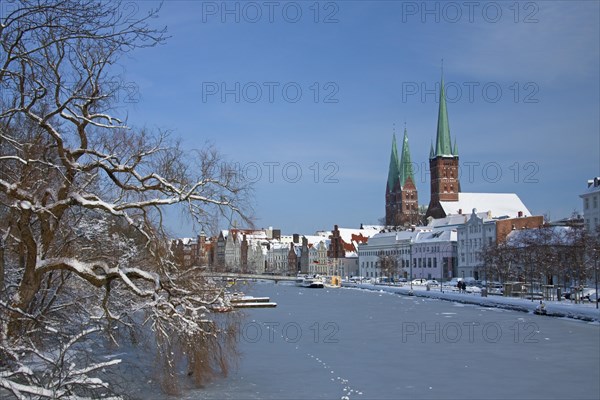 The churches of Saint Petri and Saint Mary towering above historic houses along the frozen river Trave in Luebeck in winter