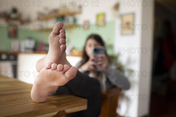 Subject: Girl sitting with feet on the table in the living room using a mobile phone