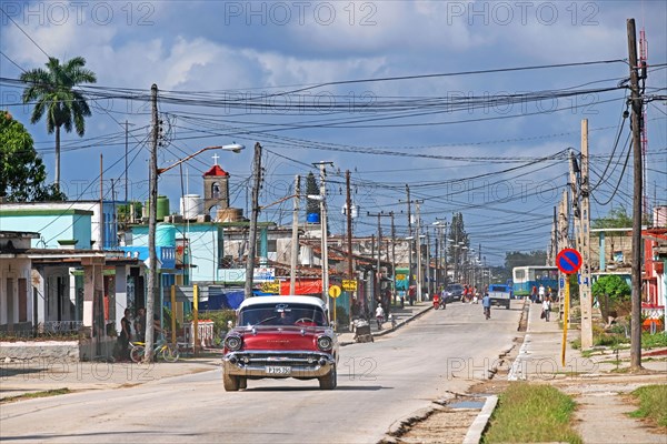 Red American classic car driving through the town Jatibonico