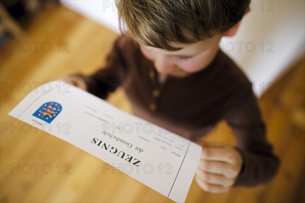 Symbolic photo on the subject of report cards in primary school. A boy poses with a report card. Berlin