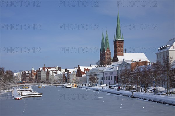 The churches of Saint Petri and Saint Mary towering above historic houses along the frozen river Trave in Luebeck in winter