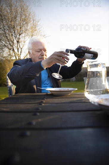 Subject: Pensioner pours himself a glass of red wine
