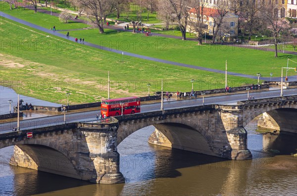 A red double-decker bus of a local city tour company crosses the Augustusbruecke