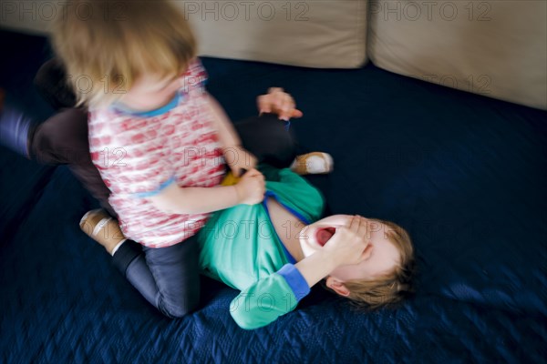 Symbolic photo on the subject of quarrels between siblings. A two-year-old girl and a five-year-old boy fight on a couch at home. Berlin