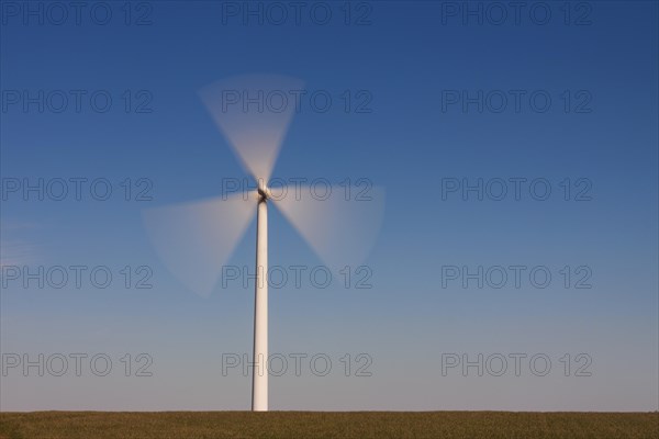 Spinning blades of windturbine in field against blue sky