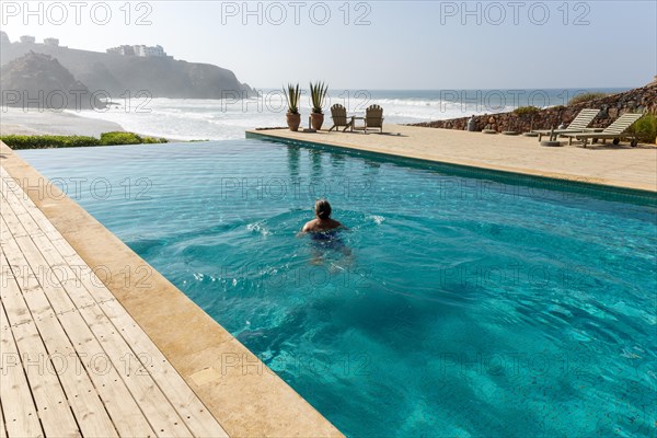 Woman swimming infinity pool by Atlantic Ocean