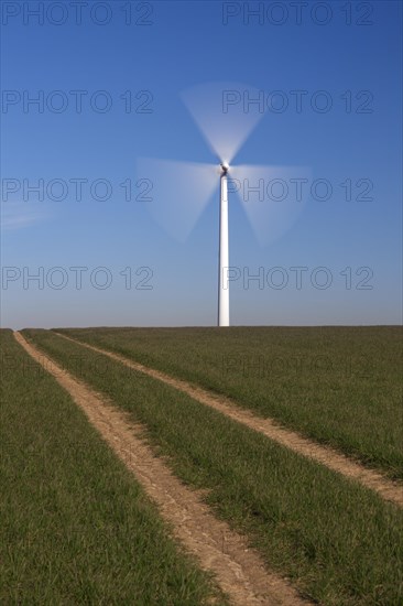 Spinning blades of windturbine in field against blue sky
