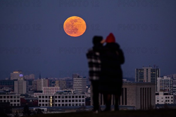 The rising full moon stands out behind the city view of Berlin