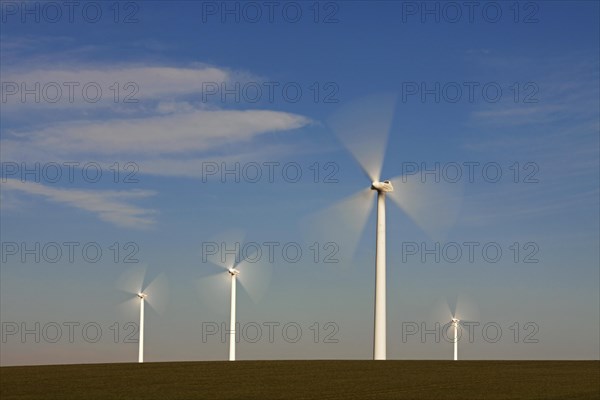 Spinning blades of wind turbines at windfarm against blue sky