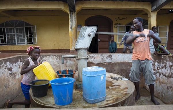 Bomeh Village at the KissyRoad rubbish dump. Girl and man at the water pump that only delivers toxic water