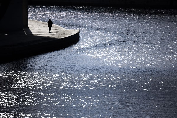 A woman stands out in the sunshine at the Spreebogen in the government district in Berlin