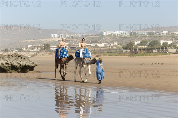 Two people riding camels on sandy beach at Taghazout