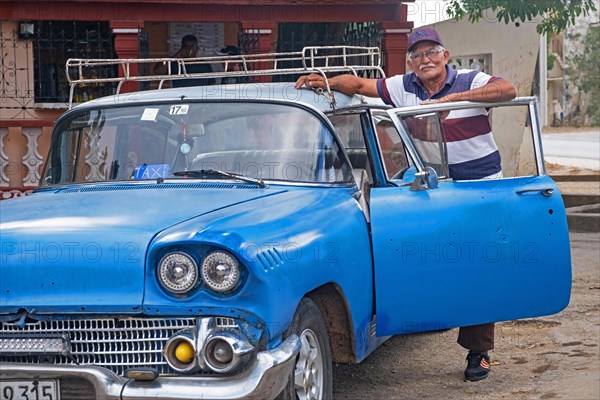 Cuban taxi driver posing with blue American classic car taxi in the city Florida