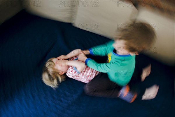 Symbolic photo on the subject of quarrels between siblings. A two-year-old girl and a five-year-old boy fight on a couch at home. Berlin