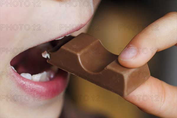 Symbolic photo on the subject of eating chocolate. A boy takes a bite from a chocolate bar. Berlin