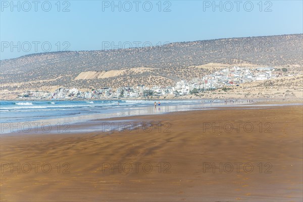 People walking along sandy beach at low tide near village of Taghazout
