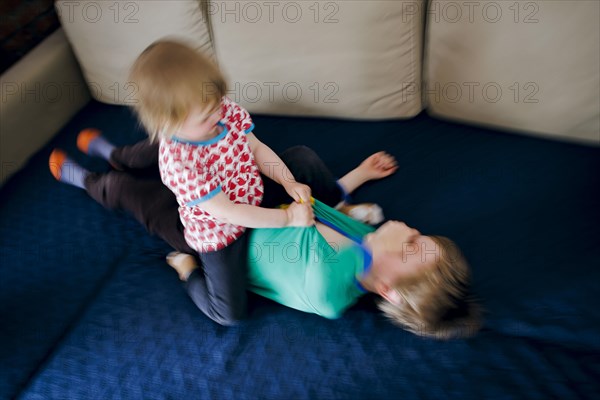 Symbolic photo on the subject of quarrels between siblings. A two-year-old girl and a five-year-old boy fight on a couch at home. Berlin