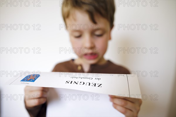 Symbolic photo on the subject of report cards in primary school. A boy poses with a report card. Berlin