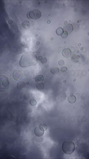 Soap bubbles are flying on gray cloudy sky background