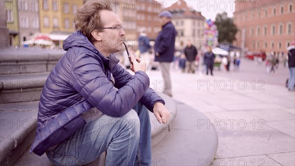Adult man sitting on square and smoking a tobacco pipe in the Palace Square