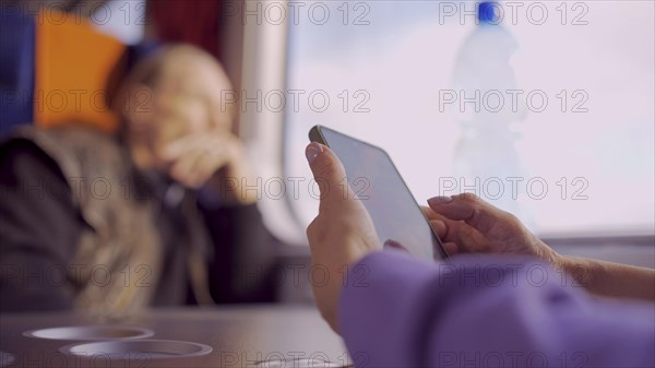 Close-up of the hands of a elderly lady sitting in a train carriageriage and using a smartphone