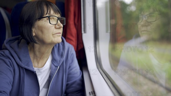 Elderly lady in glasses travels in train and looking out the window reflected in the glass