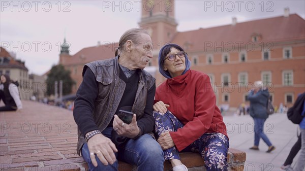 Elderly couple of tourists are sitting and talking in the historic center of an old European city