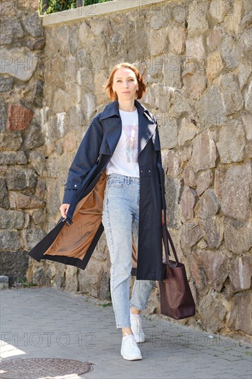 Elegant middle aged woman walks city street wearing blue trench coat