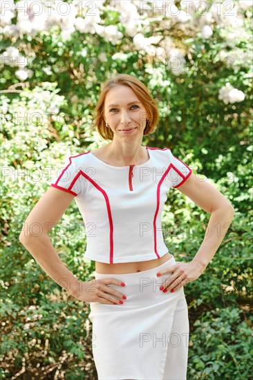 Smiling redhead woman in tennis outfit holds hands on her waist