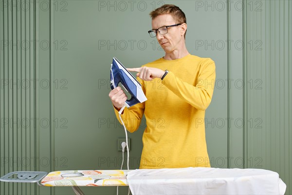 Middle aged man in spectacles touching the sole of an iron with finger