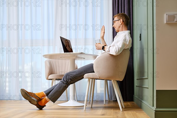 Positive middle aged man makes video call on laptop