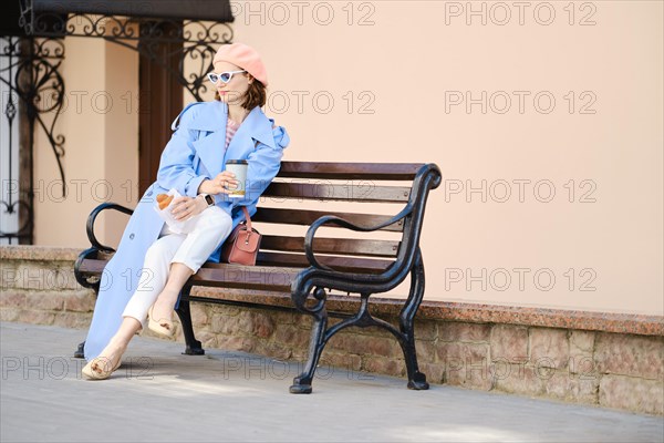 Pensive adult woman on bench with cappuccino and croissant