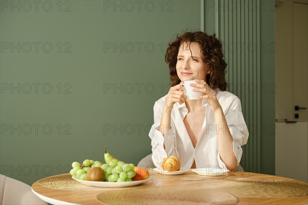 Cheerful young woman enjoying morning coffee being in dreamy and relaxed mood