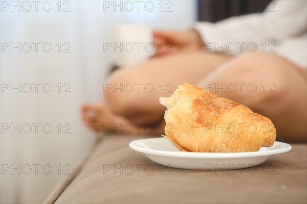 Selective focus photo of croissant with blurred female feet on a sofa in living room