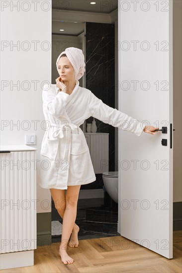 Woman in bathrobe thinking while leaving bathroom