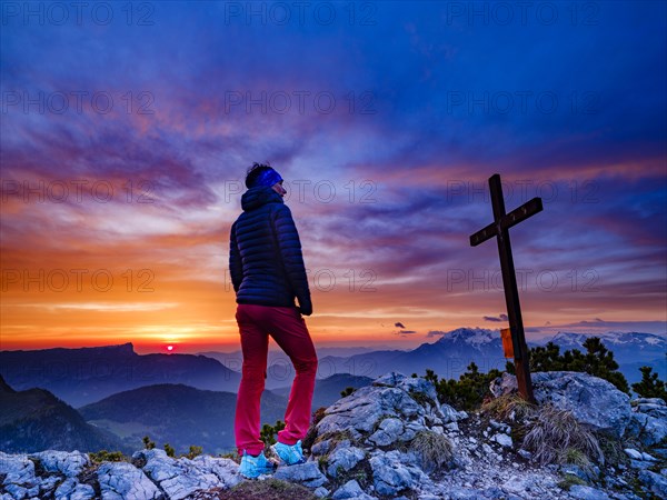 Mountaineer next to the summit cross of the iceberg and red clouds at sunrise