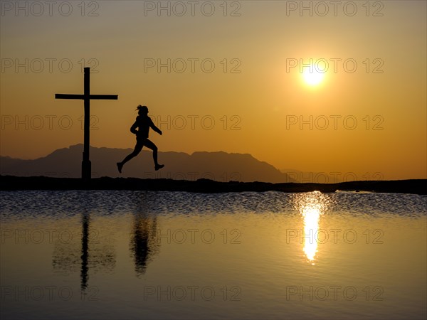 Silhouette of a runner with summit cross at sunset