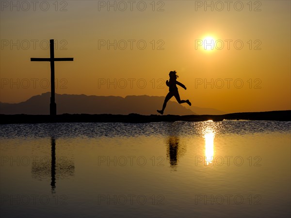 Silhouette of a runner with summit cross at sunset