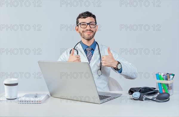 Smiling doctor sitting with laptop giving thumbs up