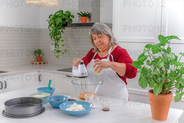 Woman chef in a white apron beating eggs in a bowl with an electric mixer to make a strawberry cake