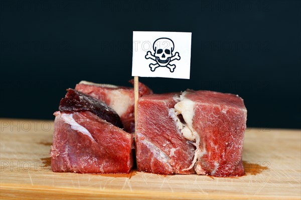 Chunks of raw meat on wooden plate with flag with poisonous skull sign