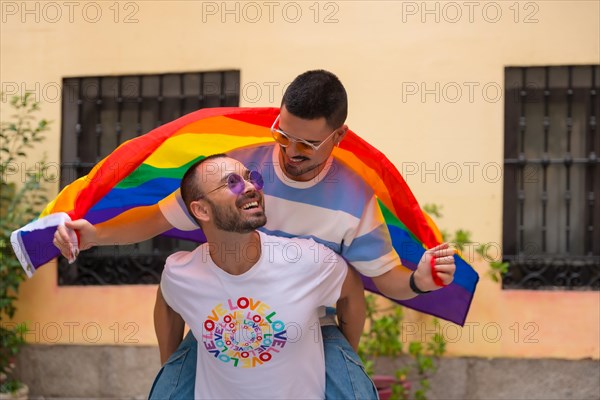 Homosexual male couple riding on back to back at pride party with rainbow flag