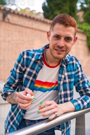 Attractive gay man painting his nails makeup with rainbow lgbt flag in the city